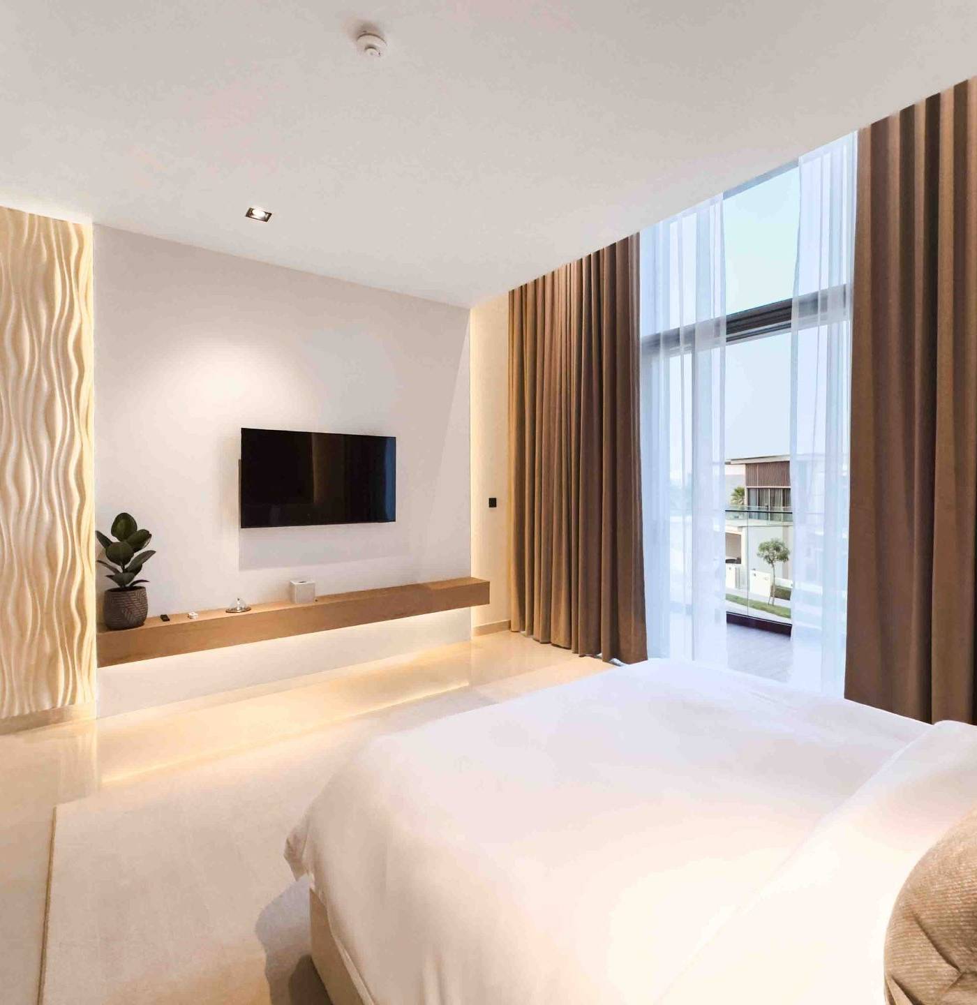 Minimalist bedroom renovation in Dubai with a large bed, wall mounted TV, floating wooden console with LED lighting and textured wave accent wall