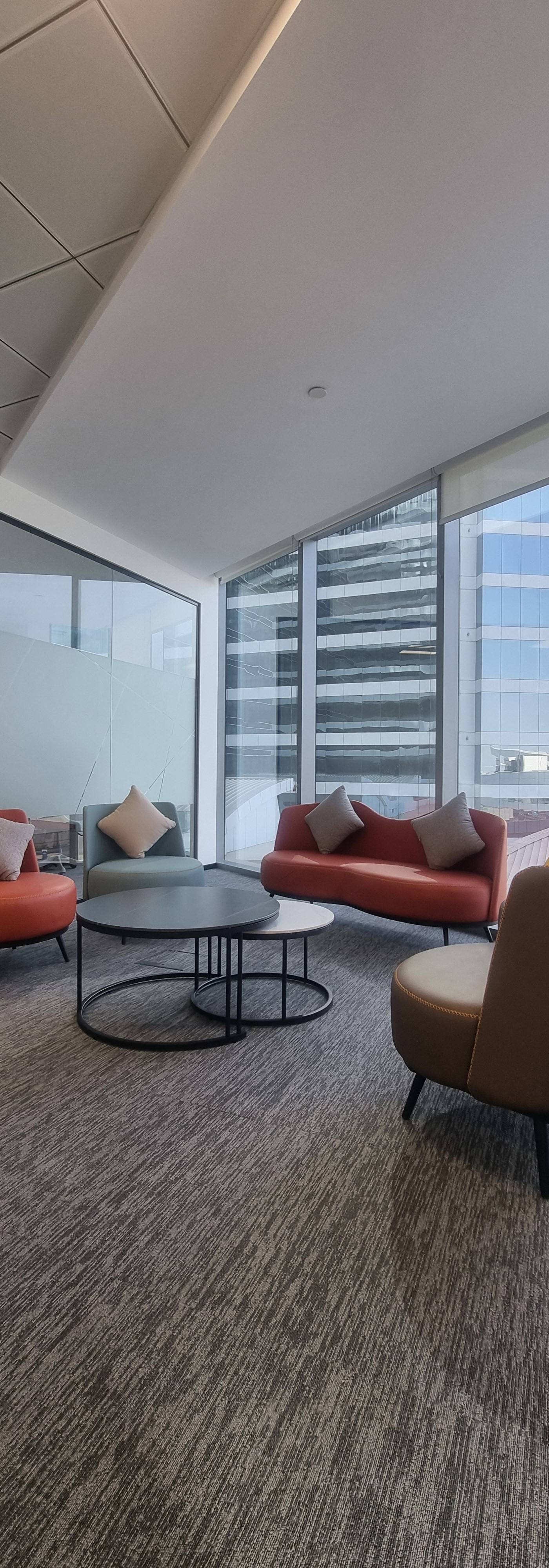 Office interior fit out in Dubai with orange, blue and brown armchairs, curved sofa, nested black coffee tables, grey carpet and floor to ceiling city view windows