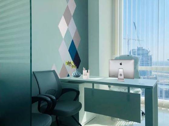 Office workstation with a teal feature wall and window view, fitted by Noor al Sundus Contracting