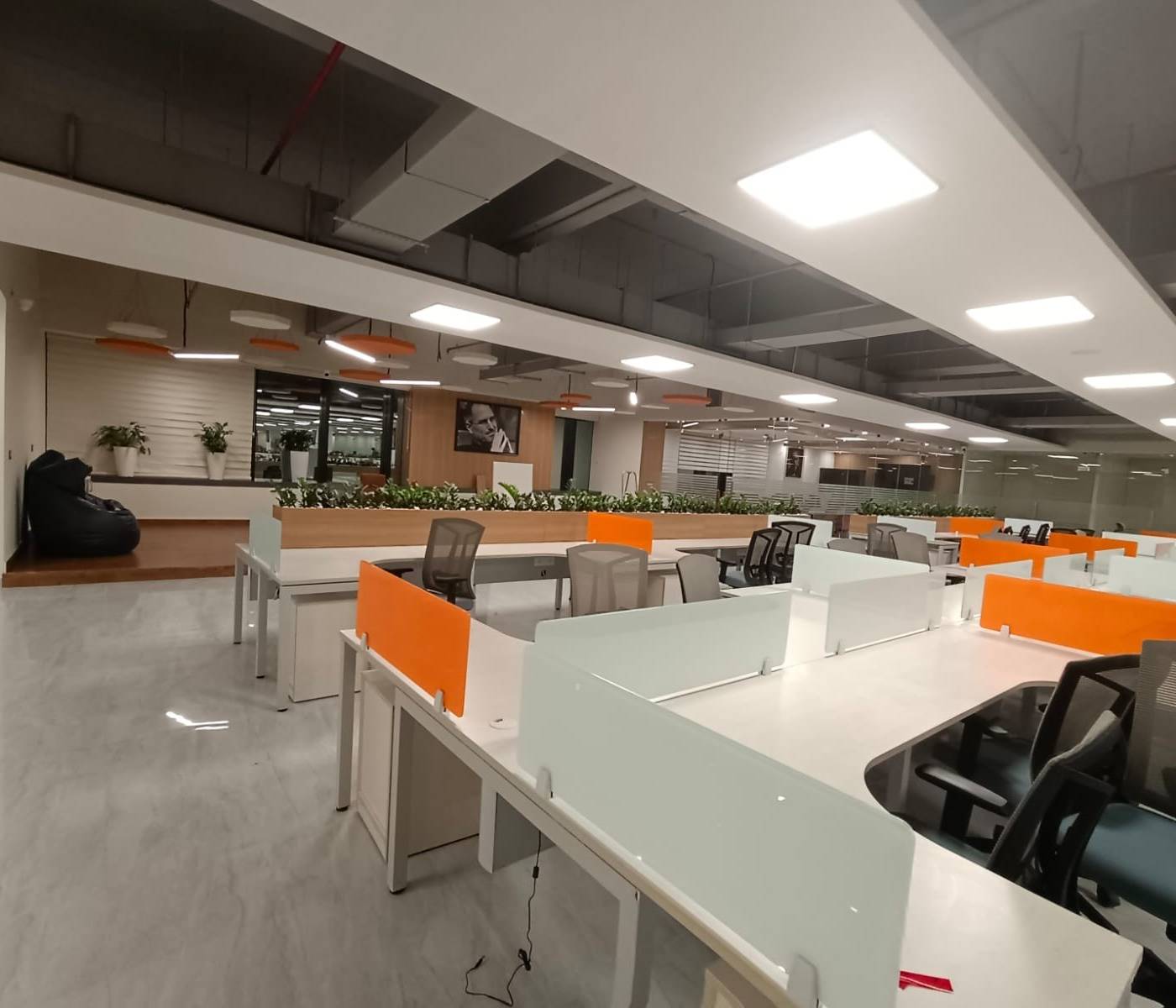 Open-plan office with white workstations, orange and white glass partitions, grey chairs and a breakout area with a black beanbag