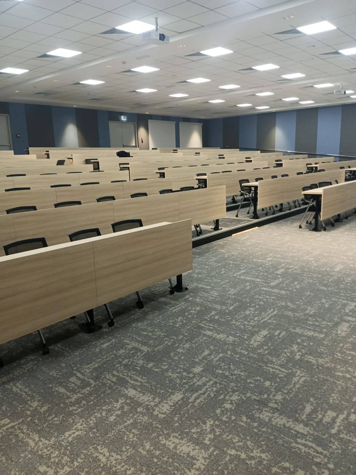 Modern lecture hall with light wood grain flip top tables and black mesh chairs fitted by Noor al Sundus in a Dubai joinery project