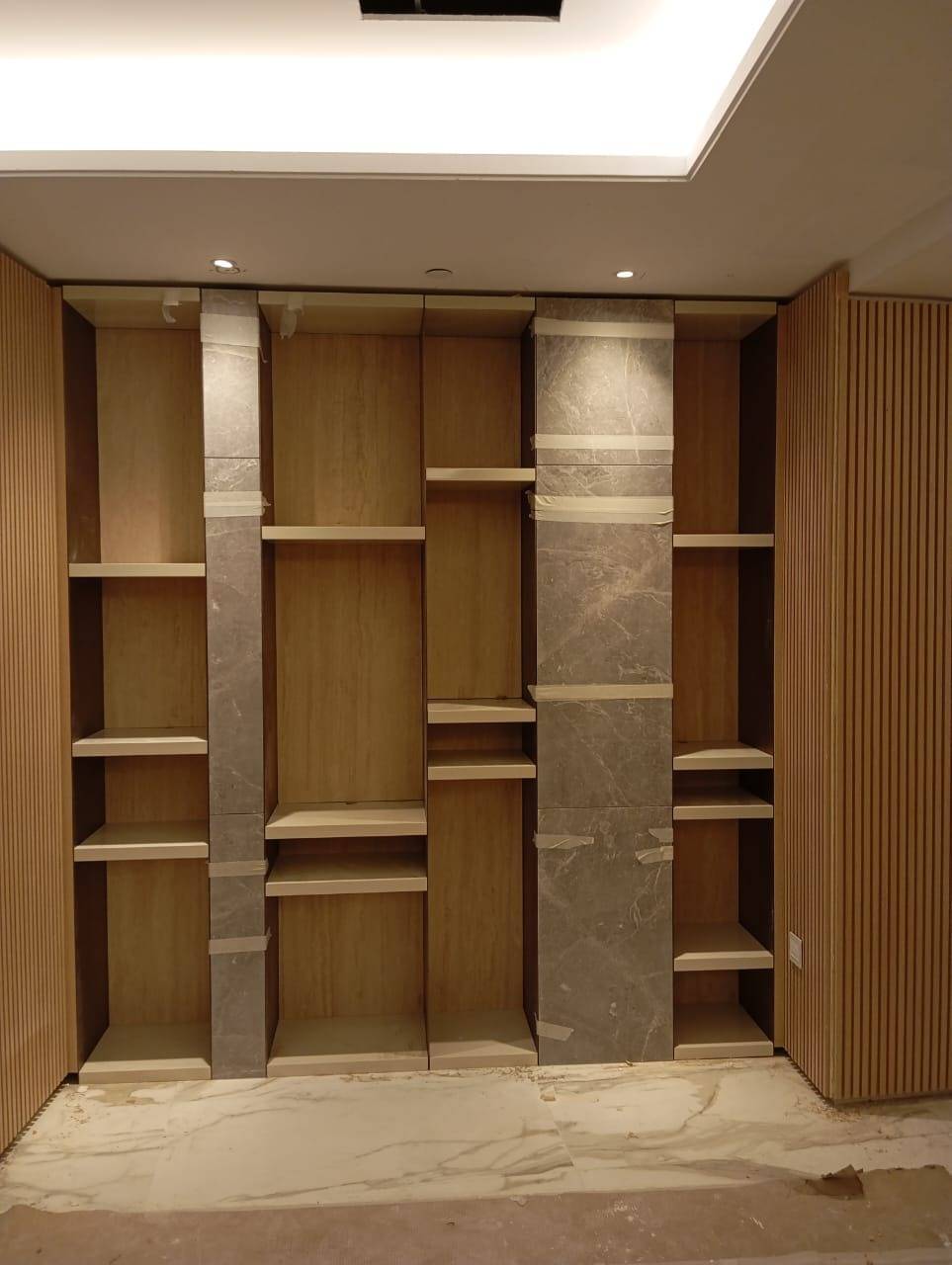 Modern built in shelving unit with light wood veneer and grey marble pillars during a Dubai fitout by Noor al Sundus