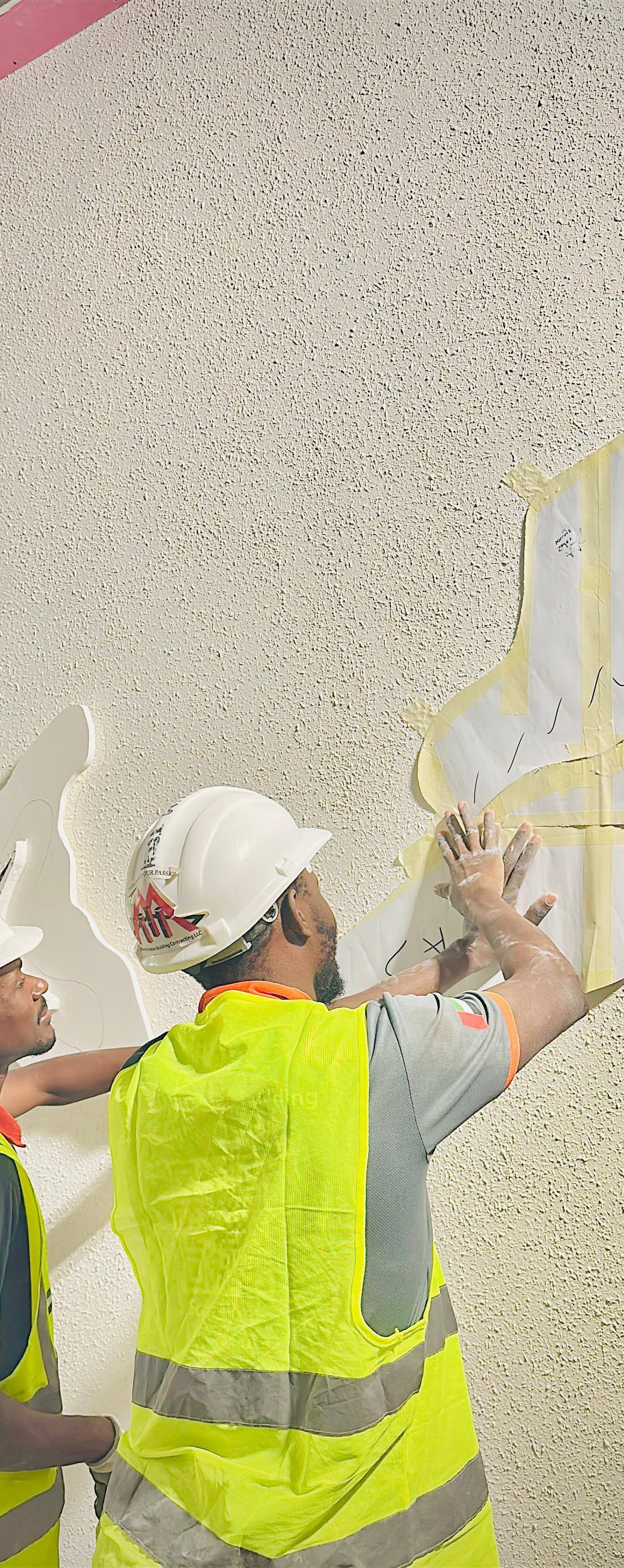 Two workers applying a paper template to a wall, precise work for a commercial renovation in Abu Dhabi.
