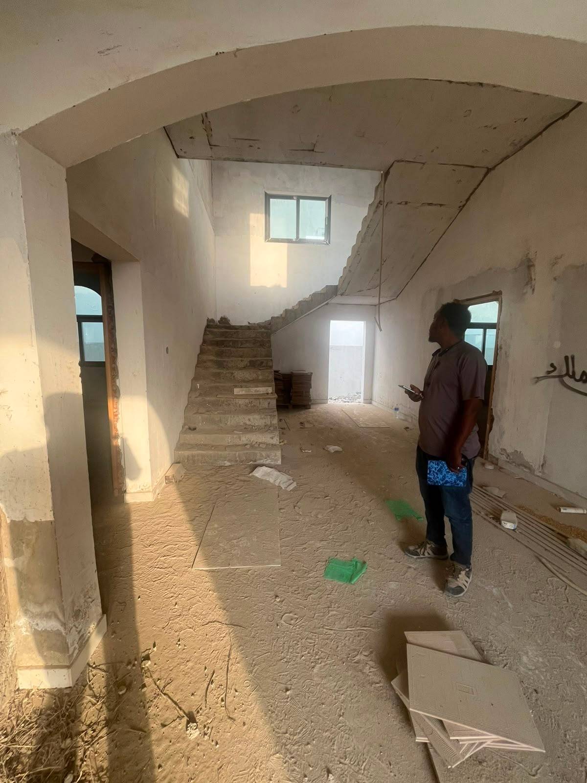 A project manager stands in a sunlit unfinished interior with a concrete staircase and exposed walls, reviewing progress during an <a href=