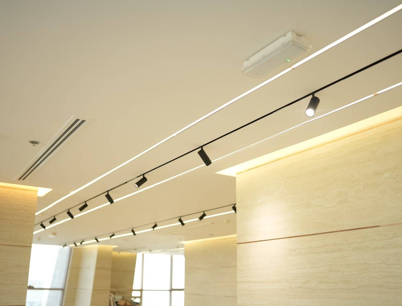 Office hallway renovation Dubai with false ceiling, linear LED lighting, and stone-clad walls.