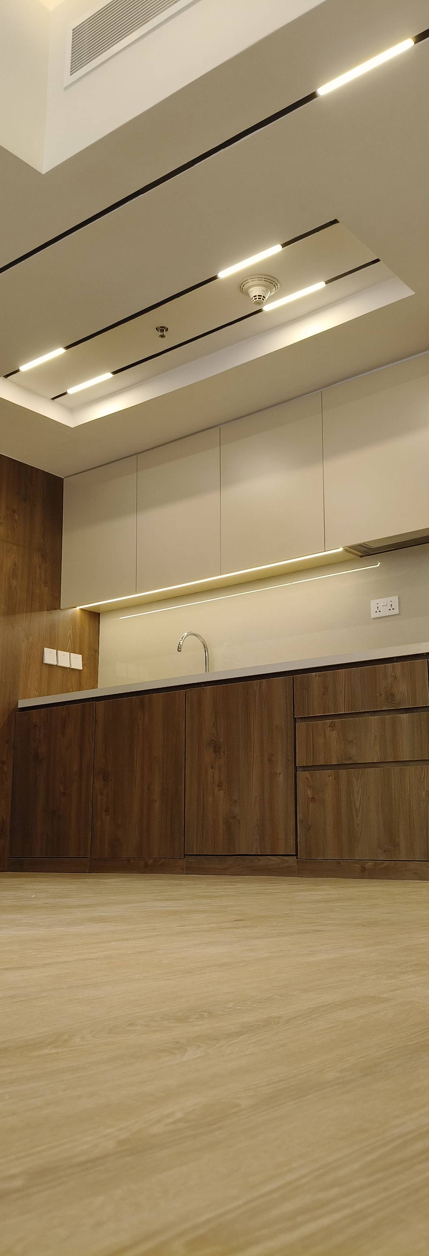 Freshly renovated modern kitchen with dark wood grain lower cabinetry, beige upper cabinets, light grey countertop with integrated sink and chrome faucet, and reeded glass display cabinet with LED strip lighting