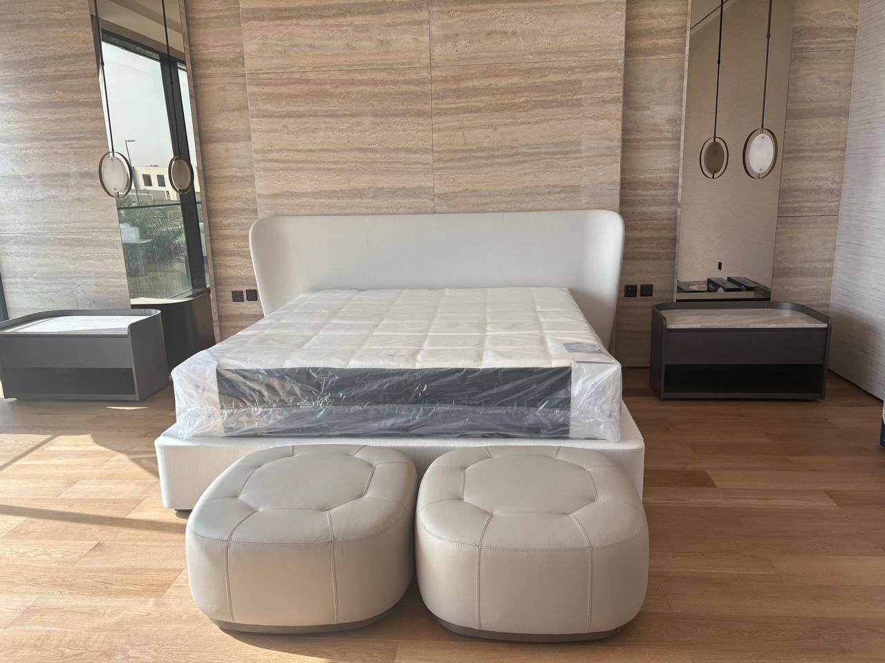Modern villa bedroom with white upholstered bed, curved headboard, dark grey integrated nightstands, and travertine feature wall, finished by LILLI PALMER BUILDING CONTRACTING