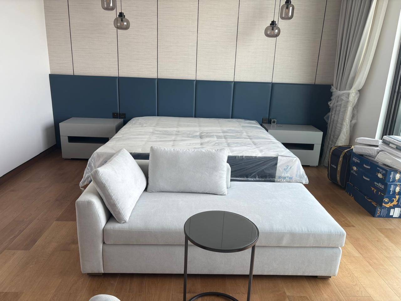 Freshly renovated bedroom with navy blue upholstered headboard, light grey chaise lounge, and floating nightstands on warm wooden flooring