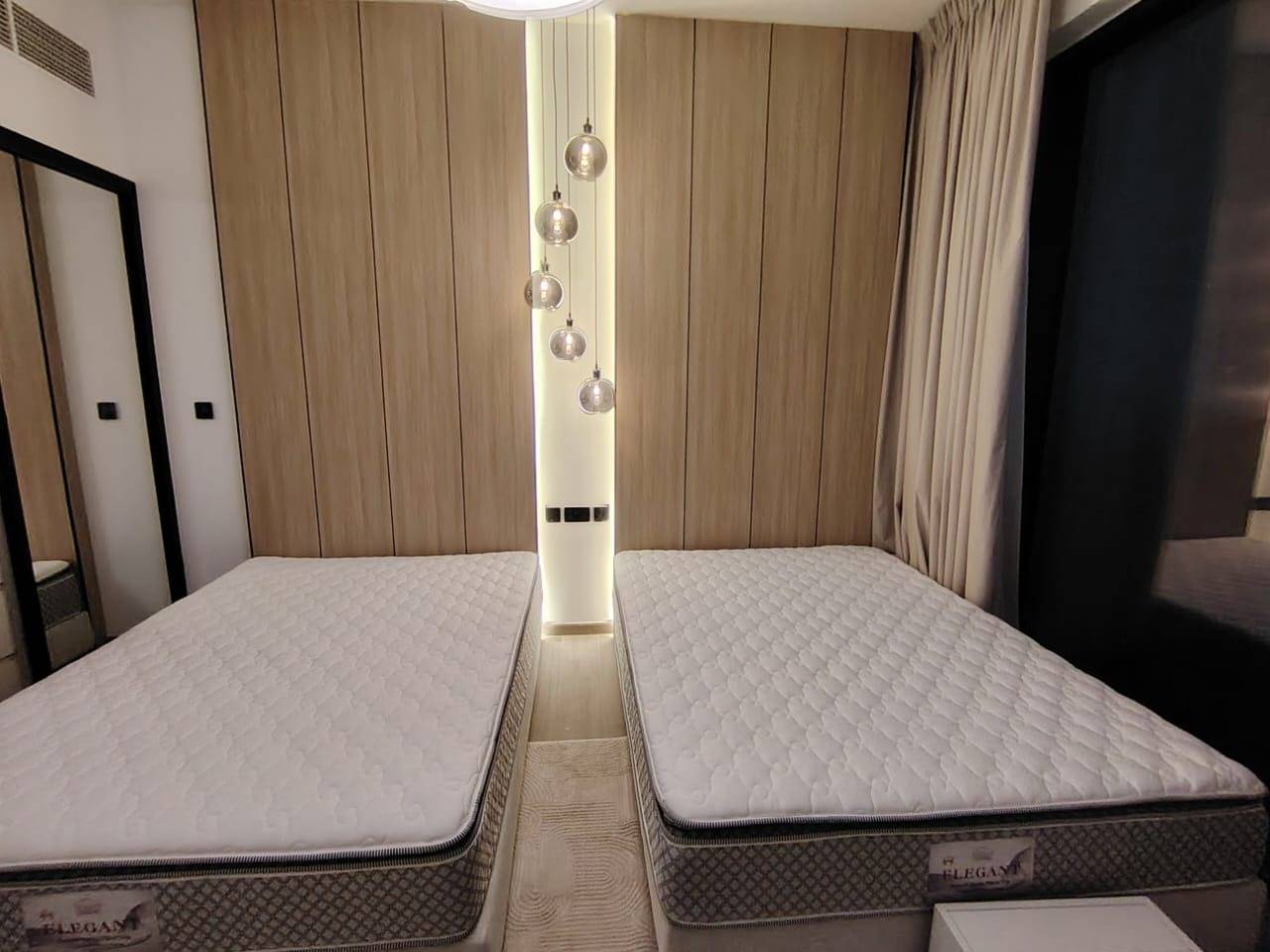 Twin bedroom with wooden panel feature wall and glass globe pendant chandelier after villa renovation