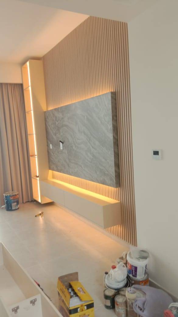 A modern The Springs villa living room with a grey marble-effect TV wall unit, light wood slats and warm LED lighting during a turnkey interior renovation
