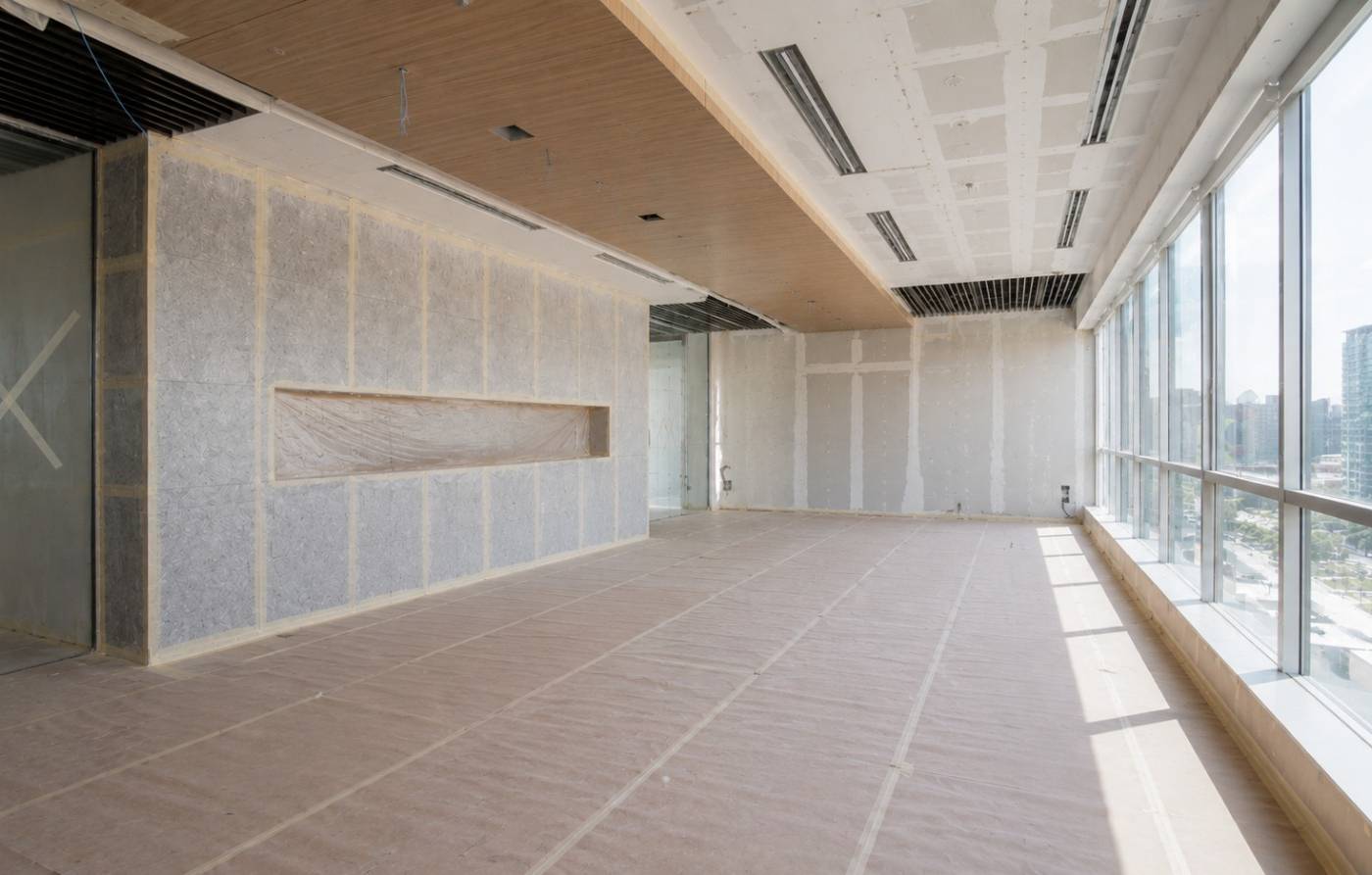 A spacious modern office interior mid renovation with partially finished drywall, acoustic wall panels, a wooden ceiling feature and floor to ceiling windows showing a city skyline