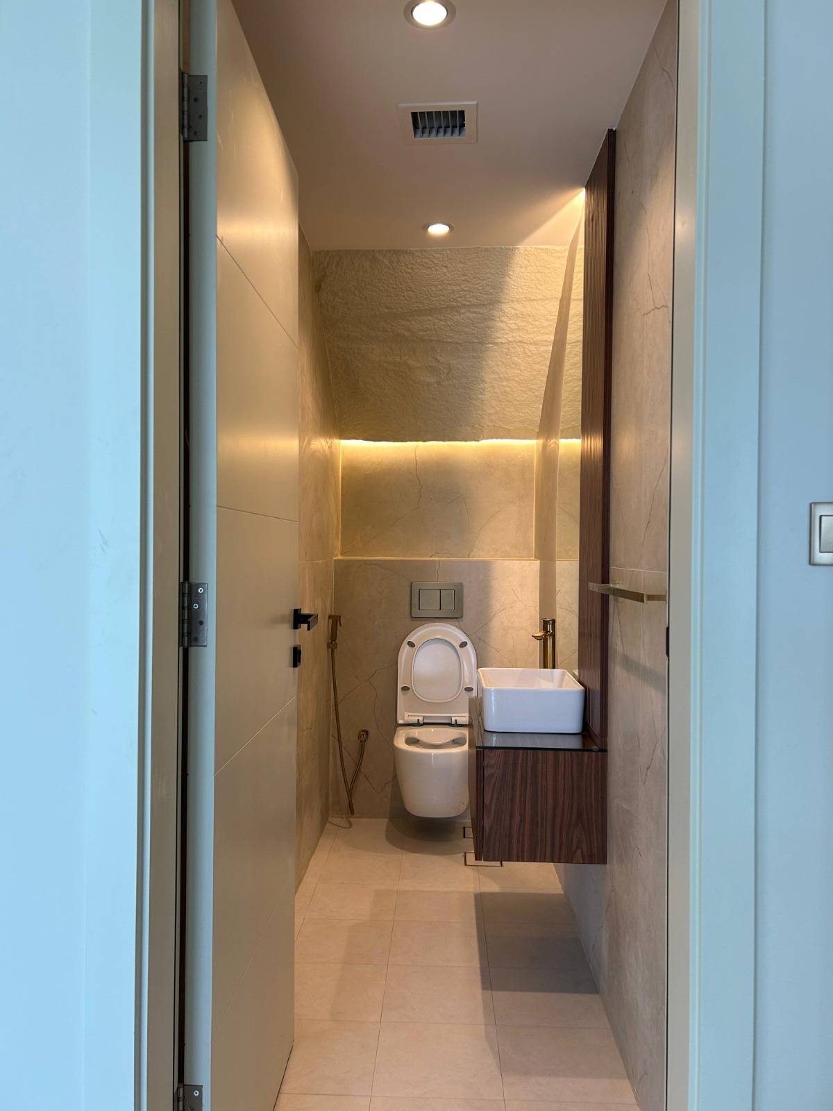 Dubai powder room with textured wall tiles, a floating dark wood vanity, white vessel sink and brass fixtures lit by LED strips, showing brass ornamentation detail work