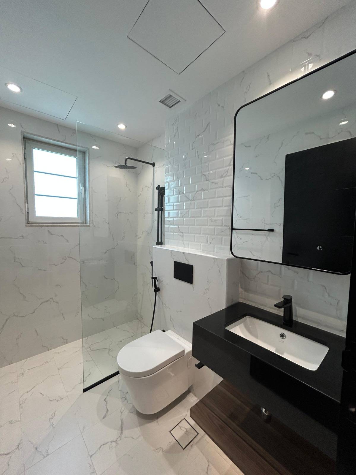 Renovated bathroom with white marble-look tiles, a subway tile feature wall and matte black fixtures, showing the matte metal finish used on custom mashrabiya screens in Dubai
