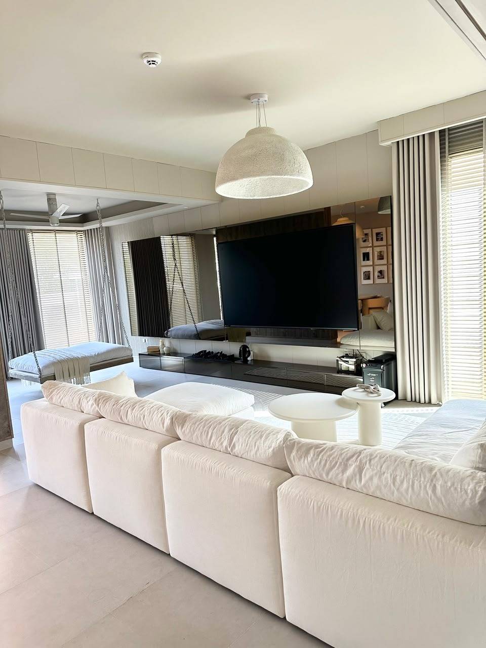 A bright and spacious modern living room in a Dubai villa renovation with white sectional sofa, wall mounted television, minimalist media console and hanging daybed