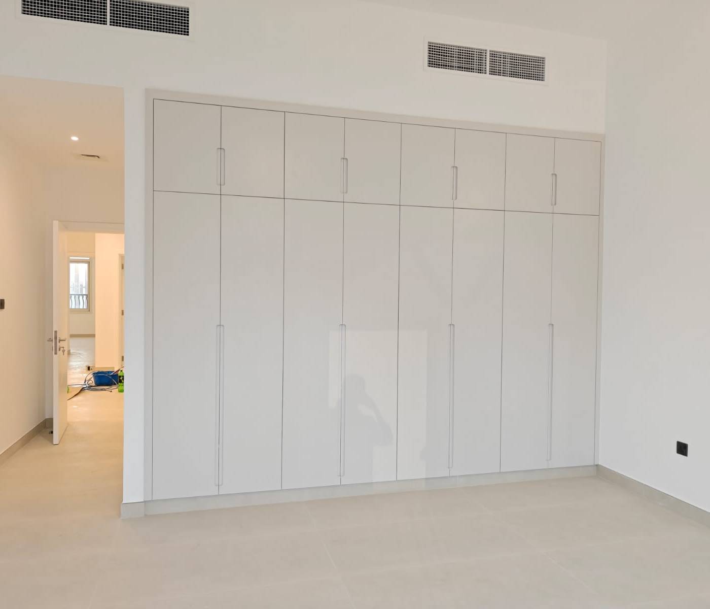 Bright empty bedroom with full wall of white glossy built-in wardrobes and tiled flooring in a refurbished Dubai villa