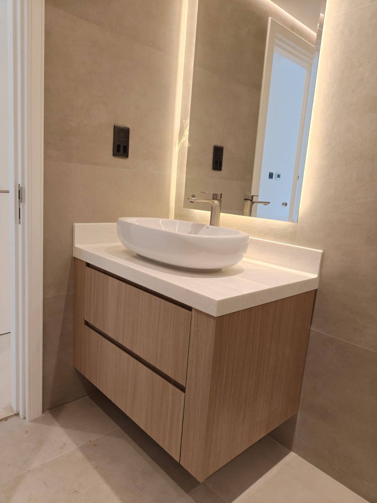 A freshly renovated modern bathroom with light wood grain floating vanity, white vessel sink, brushed nickel faucet and backlit mirror in a Dubai villa
