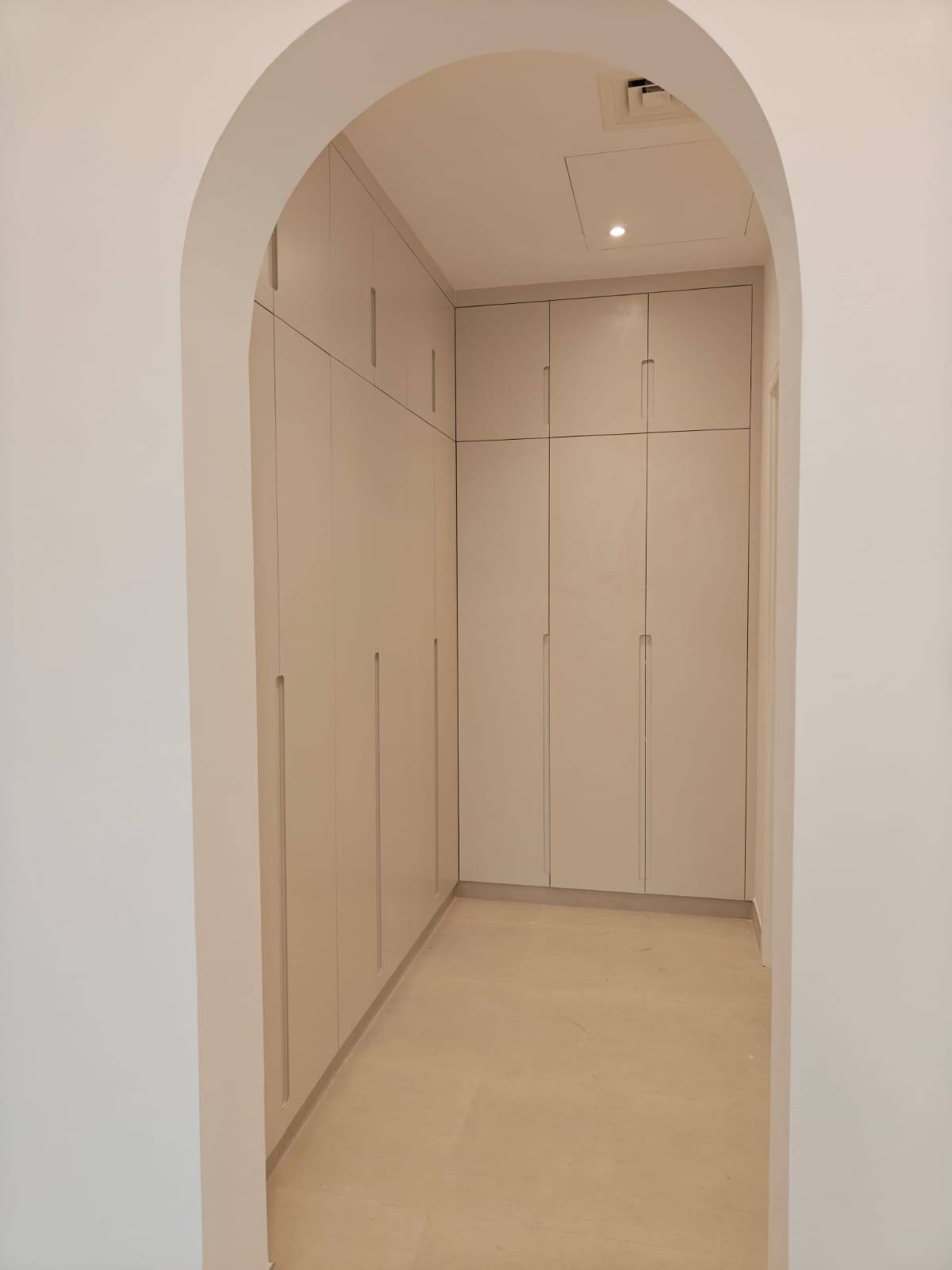 Modern minimalist Dubai villa hallway with floor-to-ceiling light greige wardrobes and arched entryway