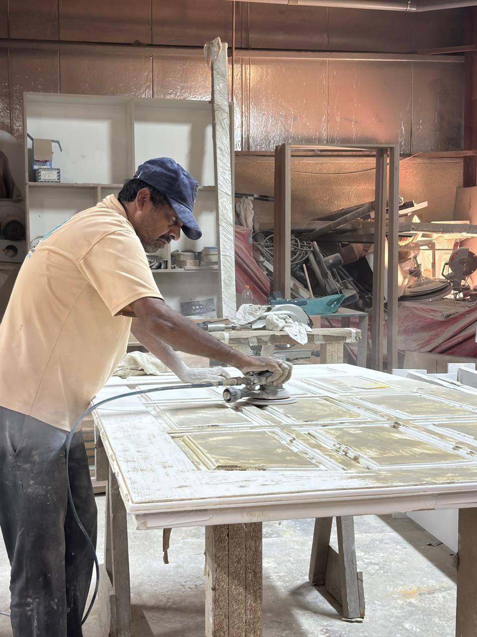 Skilled craftsman sanding a large white cabinet panel with an orbital sander during a Dubai kitchen fit-out.