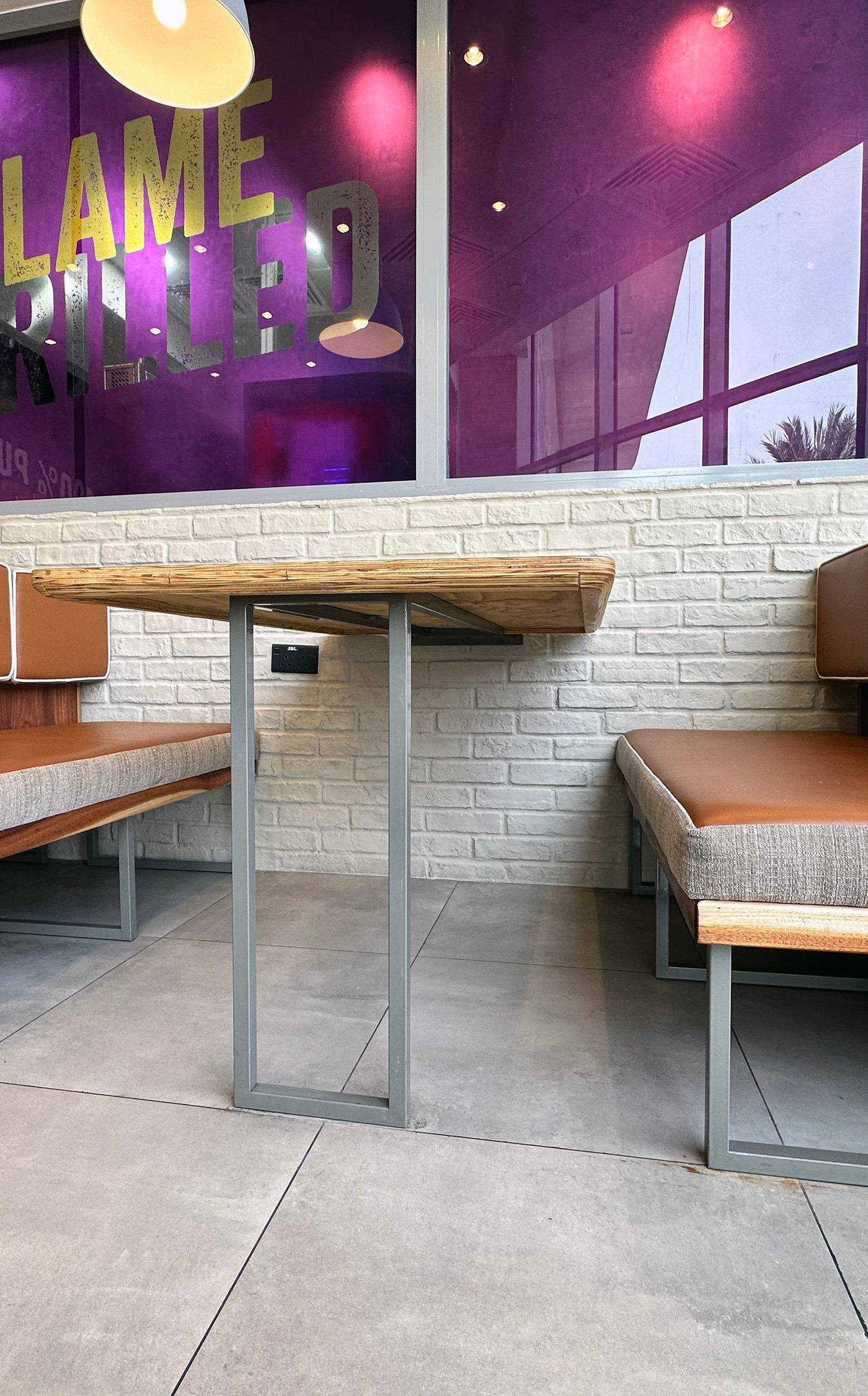 Restaurant fit out with brown leatherette booth seating, grey fabric benches, light wood tables on metal legs and a white brick wall