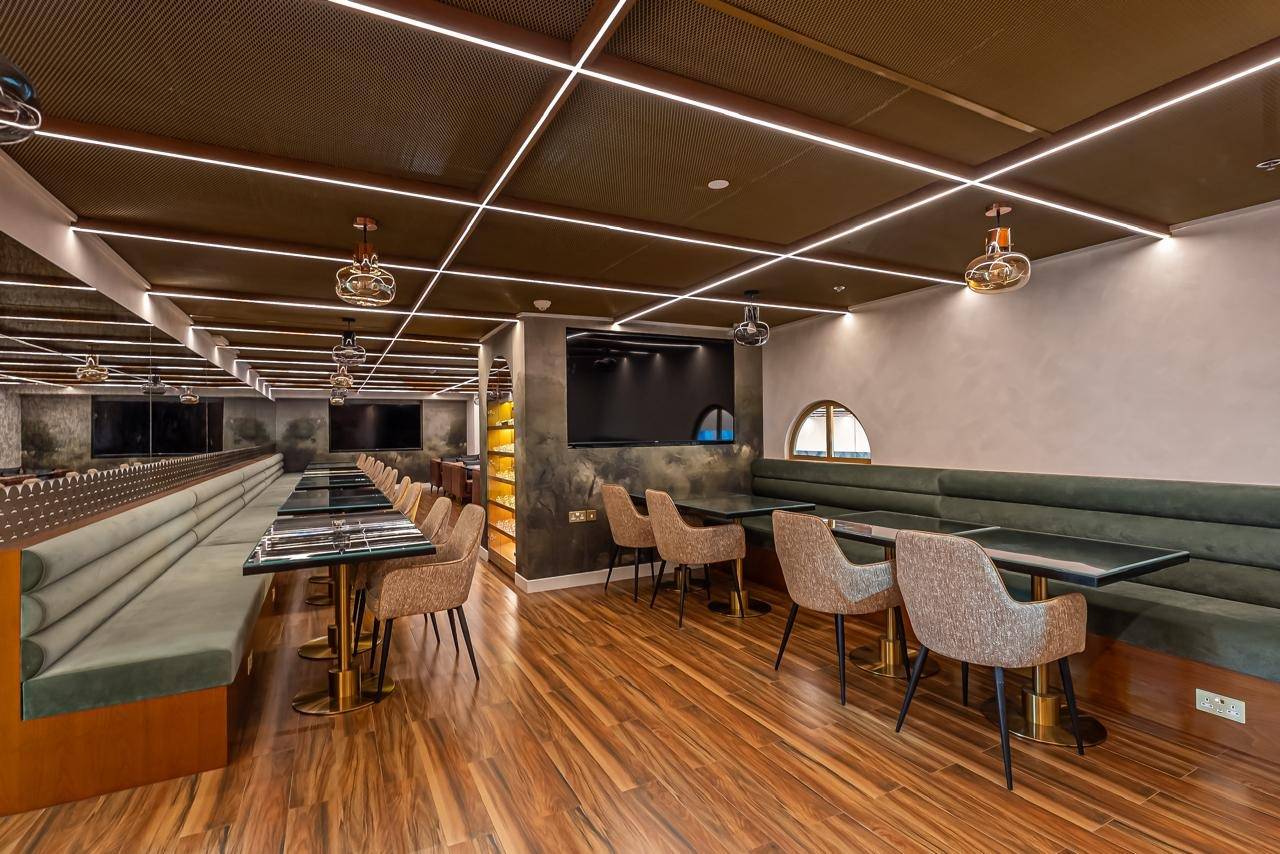 Dubai restaurant interior fit-out with long green velvet banquettes, glass top tables on brass bases, wood flooring and linear LED ceiling lights with gold pendants