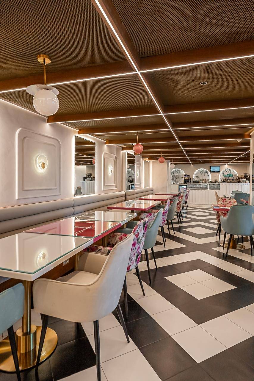 Modern cafe interior in Dubai with a black and white geometric floor, banquette seating, glass topped tables, brass fixtures and linear LED ceiling lighting