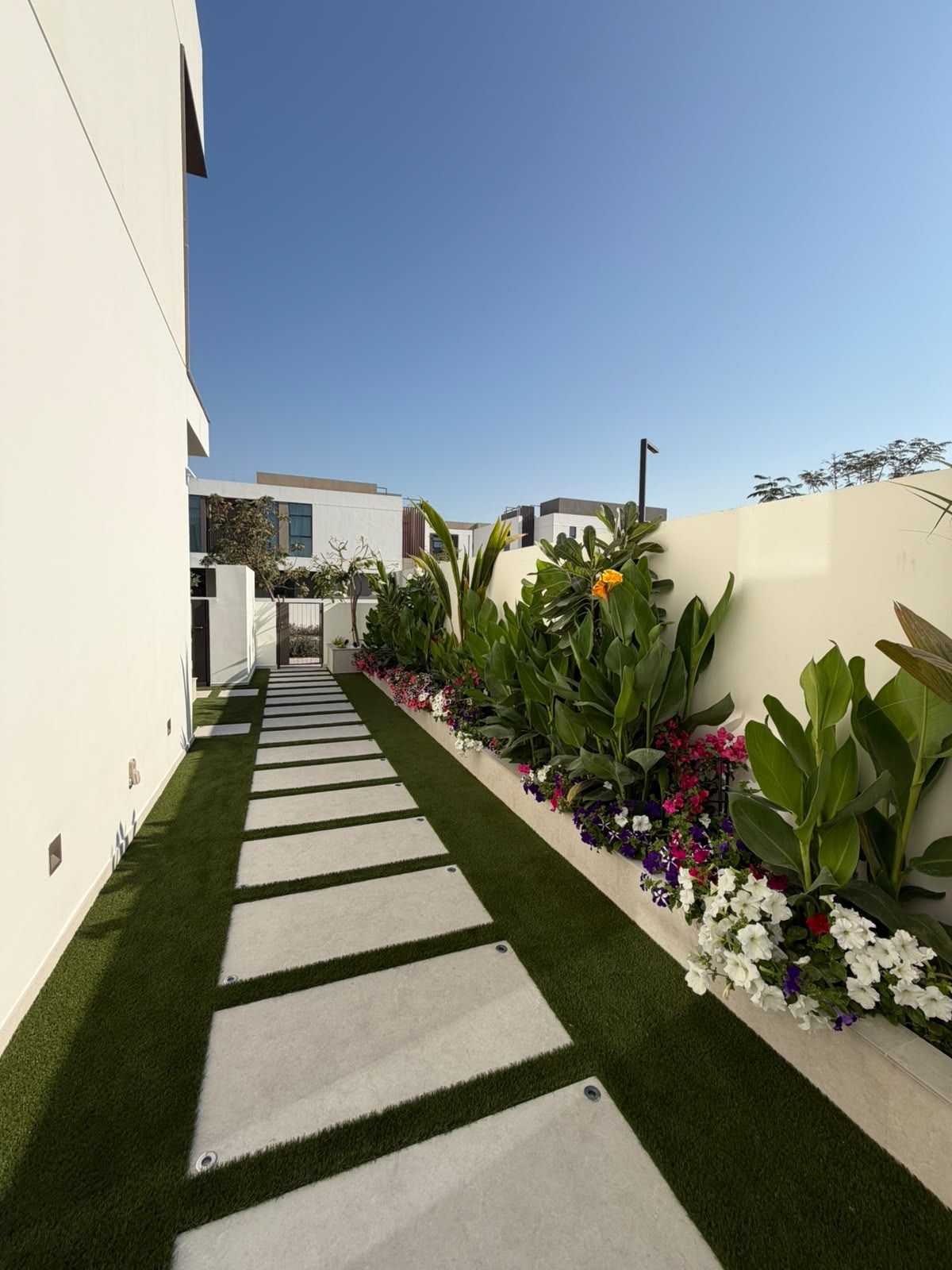 Grey stepping-stone path set in artificial grass along a villa wall