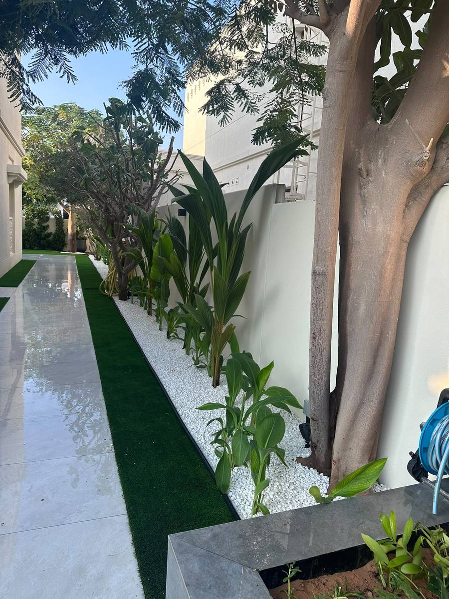 White tiled walkway beside a strip of artificial grass and planting