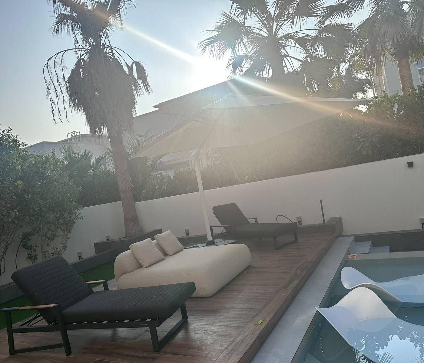 Finished villa renovation in Dubai showing a modern pool with in-water loungers, a wooden deck with black and beige seating and tropical planting under palm trees