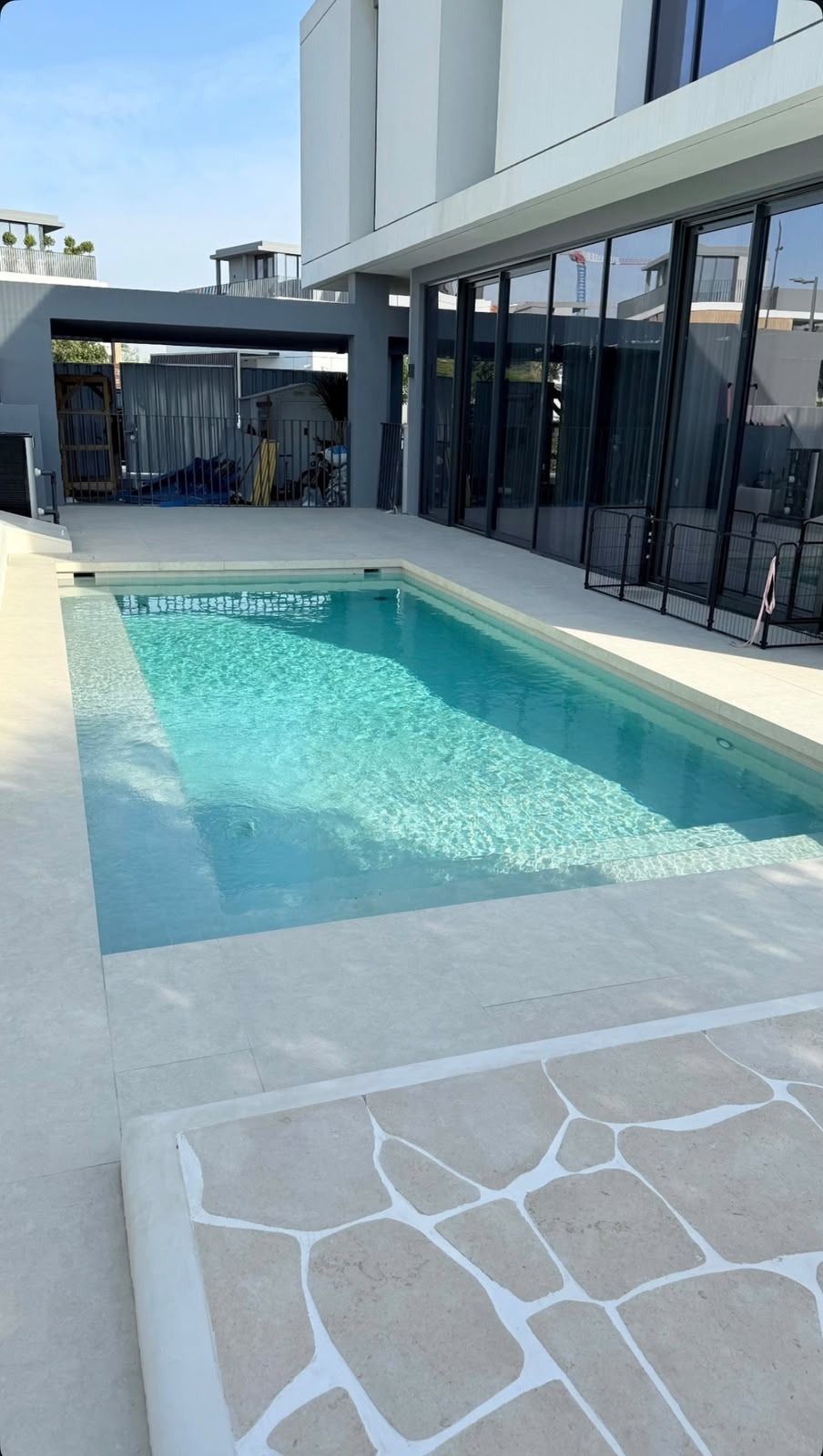 Light blue pool with white paving beside a modern villa
