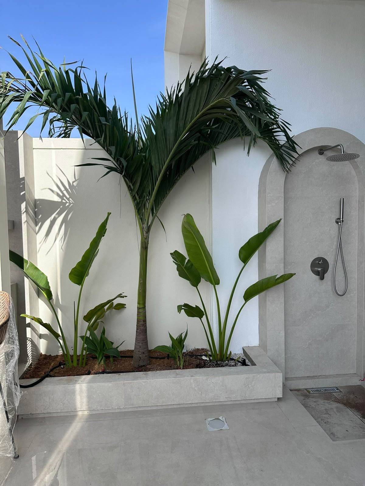 Arched outdoor shower with grey tiles beside planting