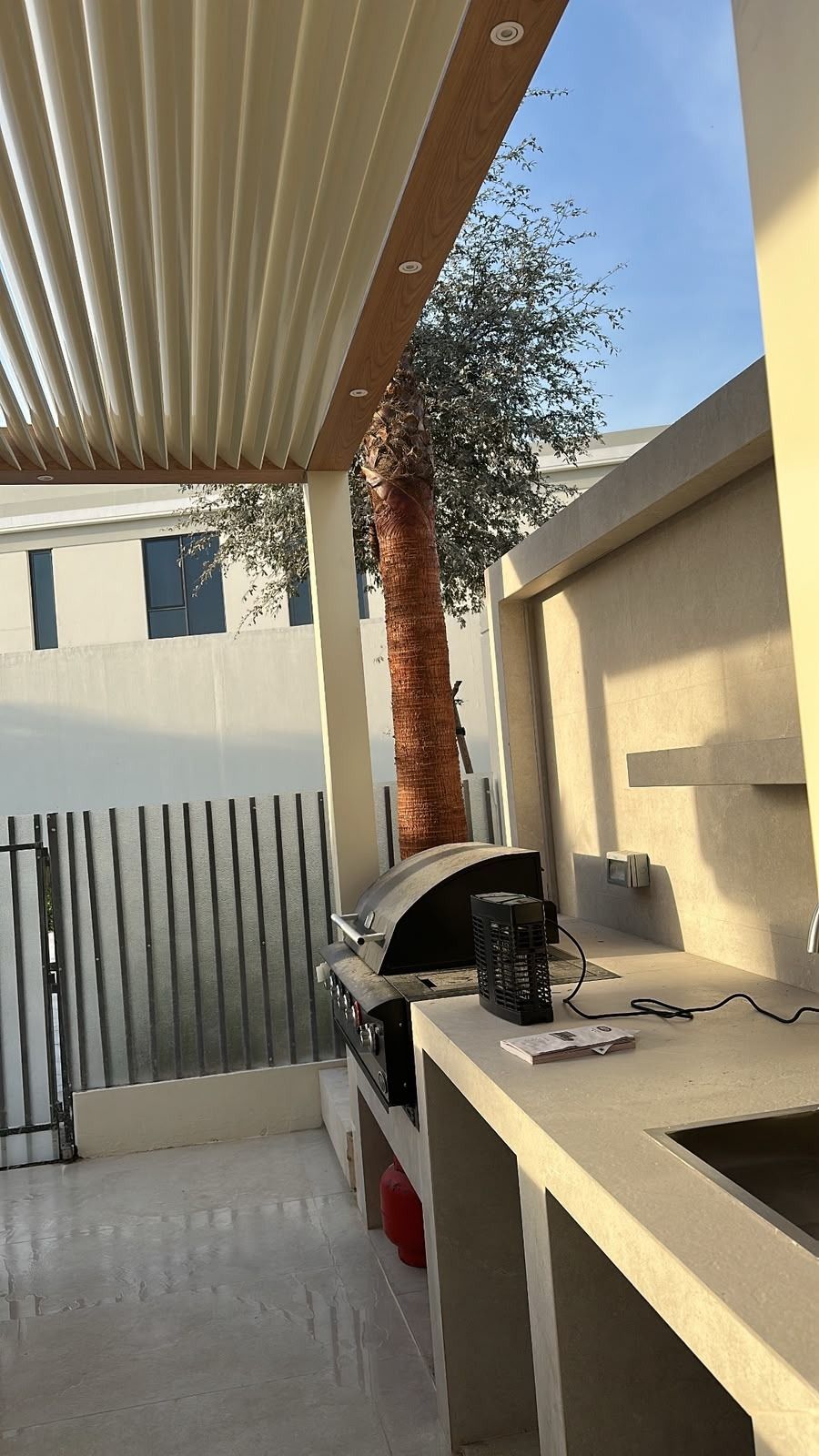 Outdoor kitchen counter with sink and grill under a pergola