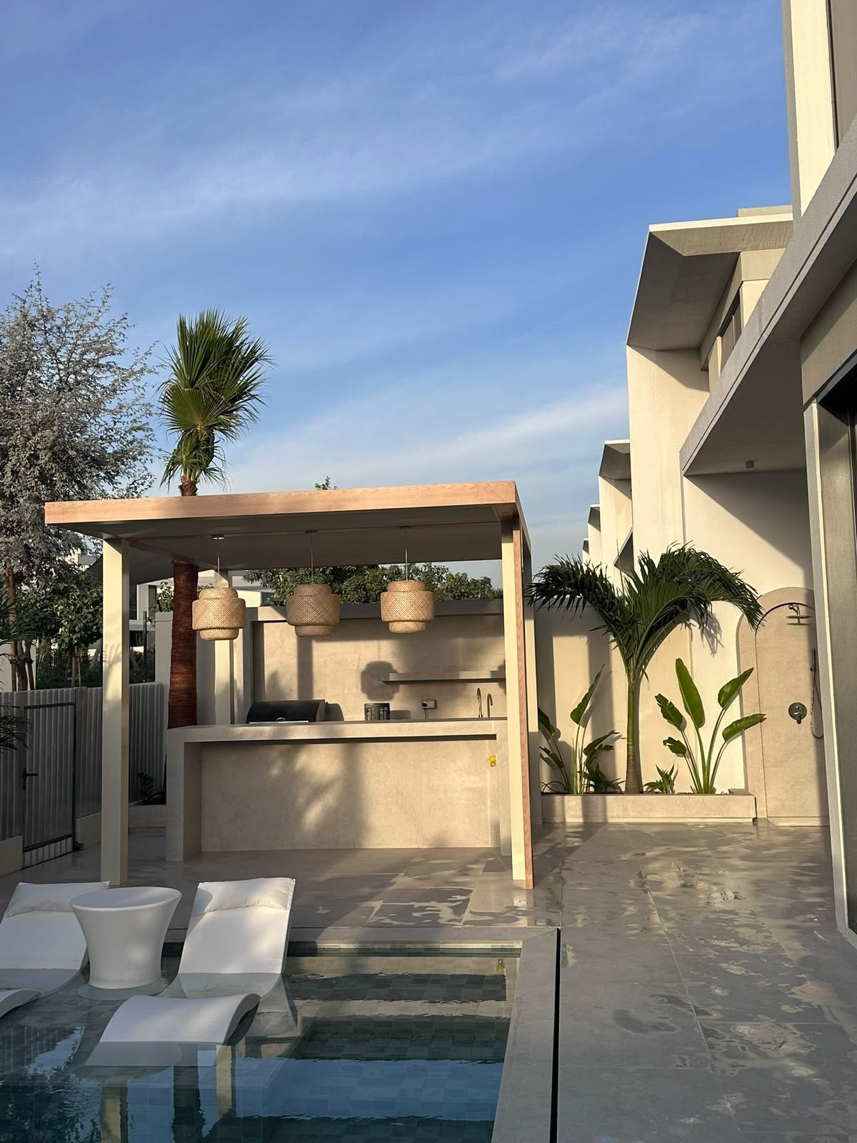 Outdoor kitchen and bar under a timber pergola beside the pool at golden hour
