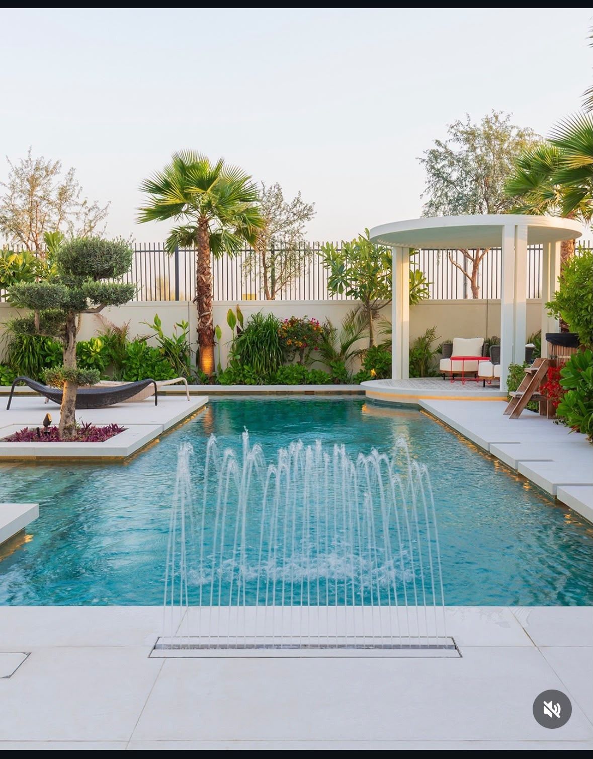 Pool with linear fountain, white paving and landscaped garden