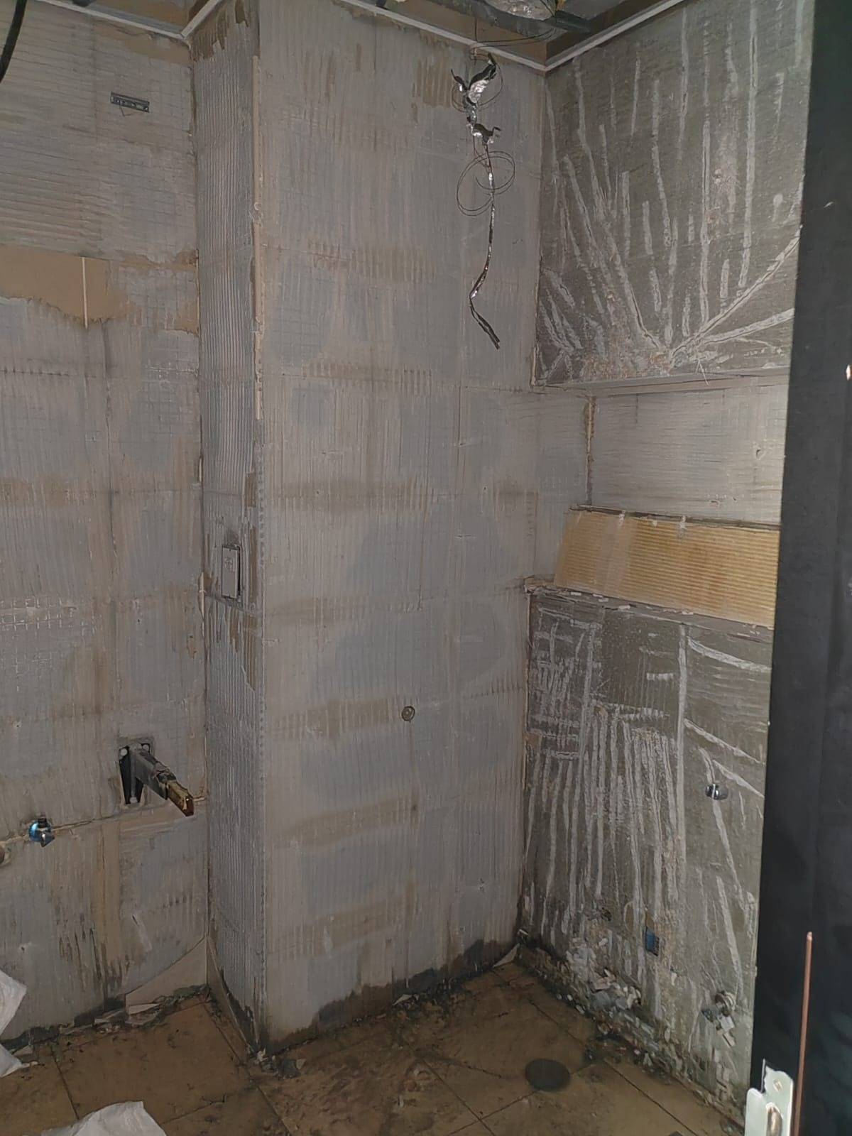 Bathroom mid renovation in Dubai with exposed plumbing and electrical wiring, textured prepared walls and a bare subfloor