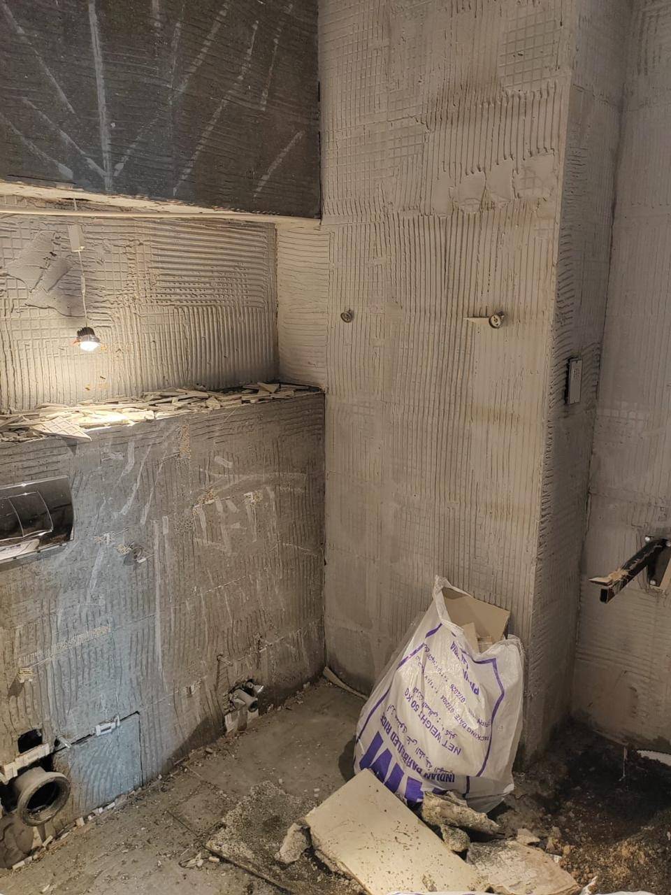 Bathroom mid renovation in Dubai with tile adhesive patterns on the walls, exposed plumbing rough-ins and construction debris under a single temporary light